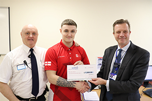 Alex Collier receives a cheque from HMP Forest Bank Director Matt Spencer alongside his father, Keith